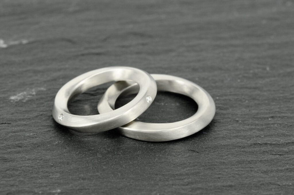 Paar Eheringe aus kühlem Platin in Möbius-Form von Goldschmiede Stephanie Berger, Damenring mit brillantbesetzter Drehung.