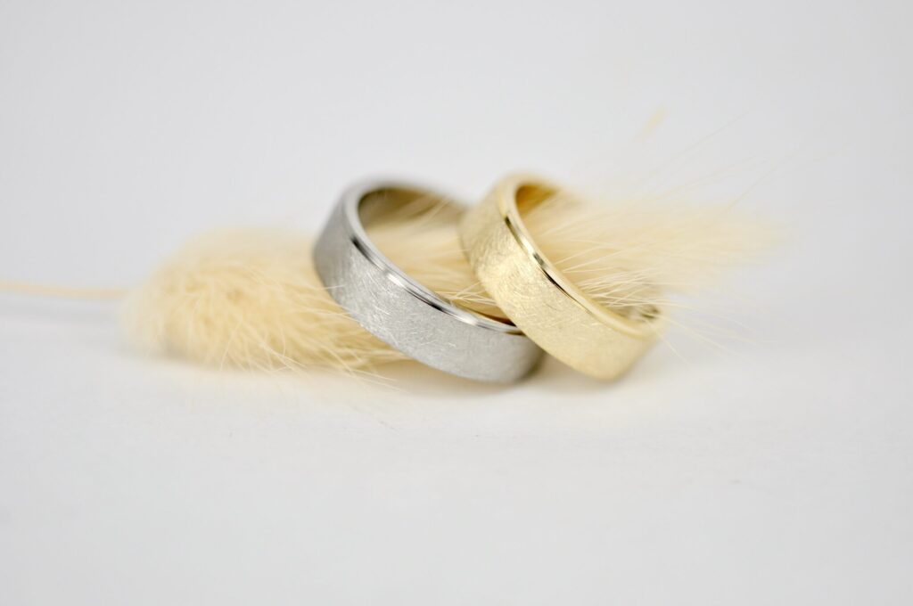 Paar Eheringe von Goldschmiede Stephanie Berger mit mattierter Oberfläche und hochglanzpolierter Glanzkante – Herrenring in Weißgold, Damenring in Gelbgold.