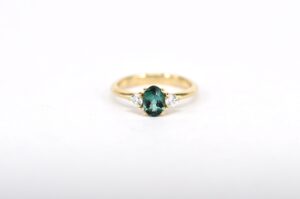 Individuell angefertigter Trilogie-Verlobungsring von Goldschmiede Stephanie Berger mit einem zentralen, oval geschliffenen grünen Turmalin und zwei seitlichen Edelsteinen.