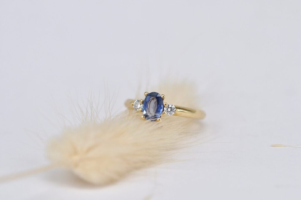 Handgefertigter Trilogie-Ring aus Echtgold von Goldschmiede Stephanie Berger mit einem zentralen, oval geschliffenen blauen Saphir und zwei flankierenden Brillanten.