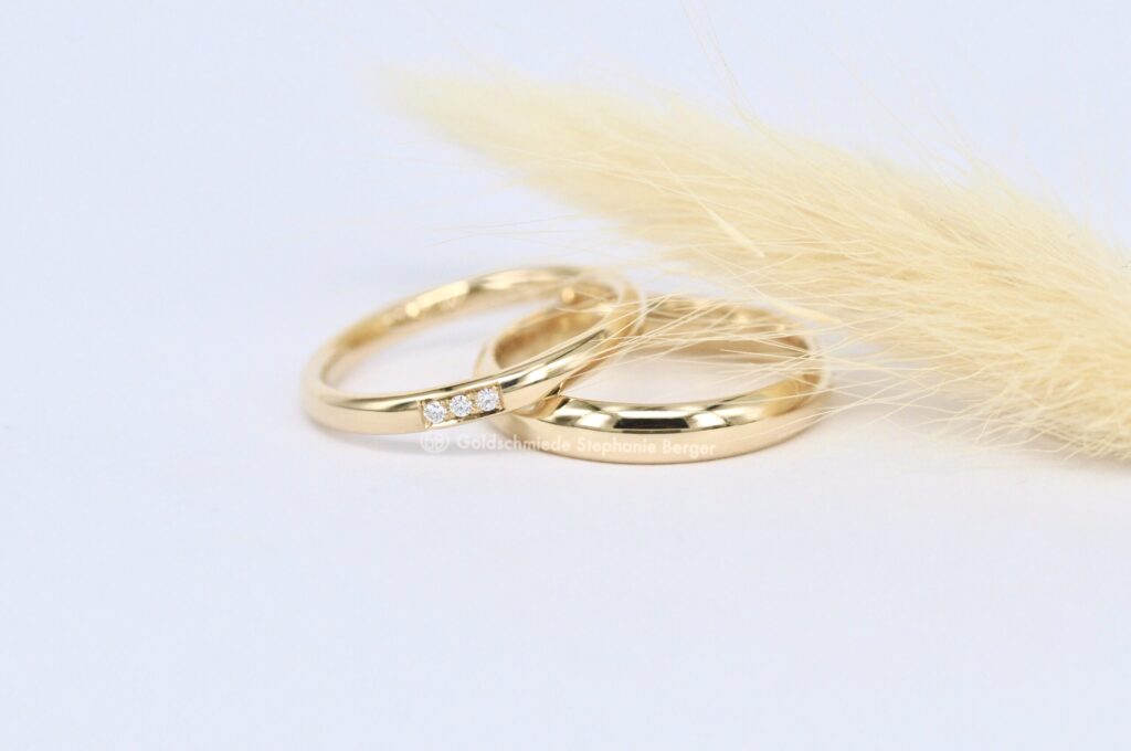 Paar Eheringe aus Gelbgold von Goldschmiede Stephanie Berger, der Damenring besetzt mit drei Brillanten.
