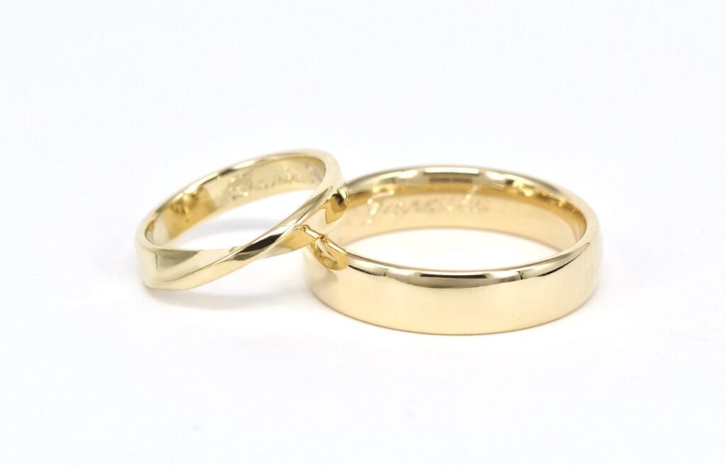 Paar Trauringe aus warmem Gelbgold von Goldschmiede Stephanie Berger, Damenring in eleganter Möbius-Form mit charakteristischer Drehung.