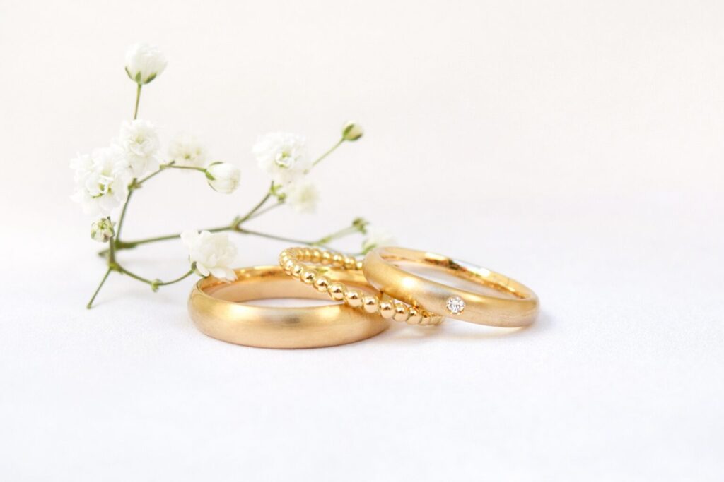 Schlichte Eheringe aus fein mattiertem 750 Gelbgold von Goldschmiede Stephanie Berger, kombiniert mit einem filigranen Kugel-Beisteckring für die Dame.