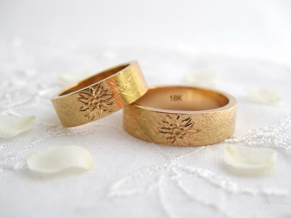 Paar handgefertigter Trauringe aus Gold von Goldschmiede Stephanie Berger mit filigraner Edelweiß-Gravur auf der Ringaußenseite.
