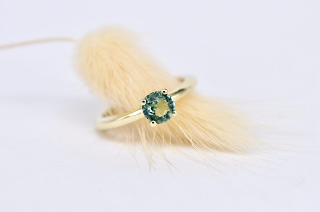 Ein eleganter Verlobungsring aus Gelbgold mit einem funkelnden, farbigen Edelstein in einer klassischen Krappen-Fassung, handgefertigt von Goldschmiede Stephanie Berger.